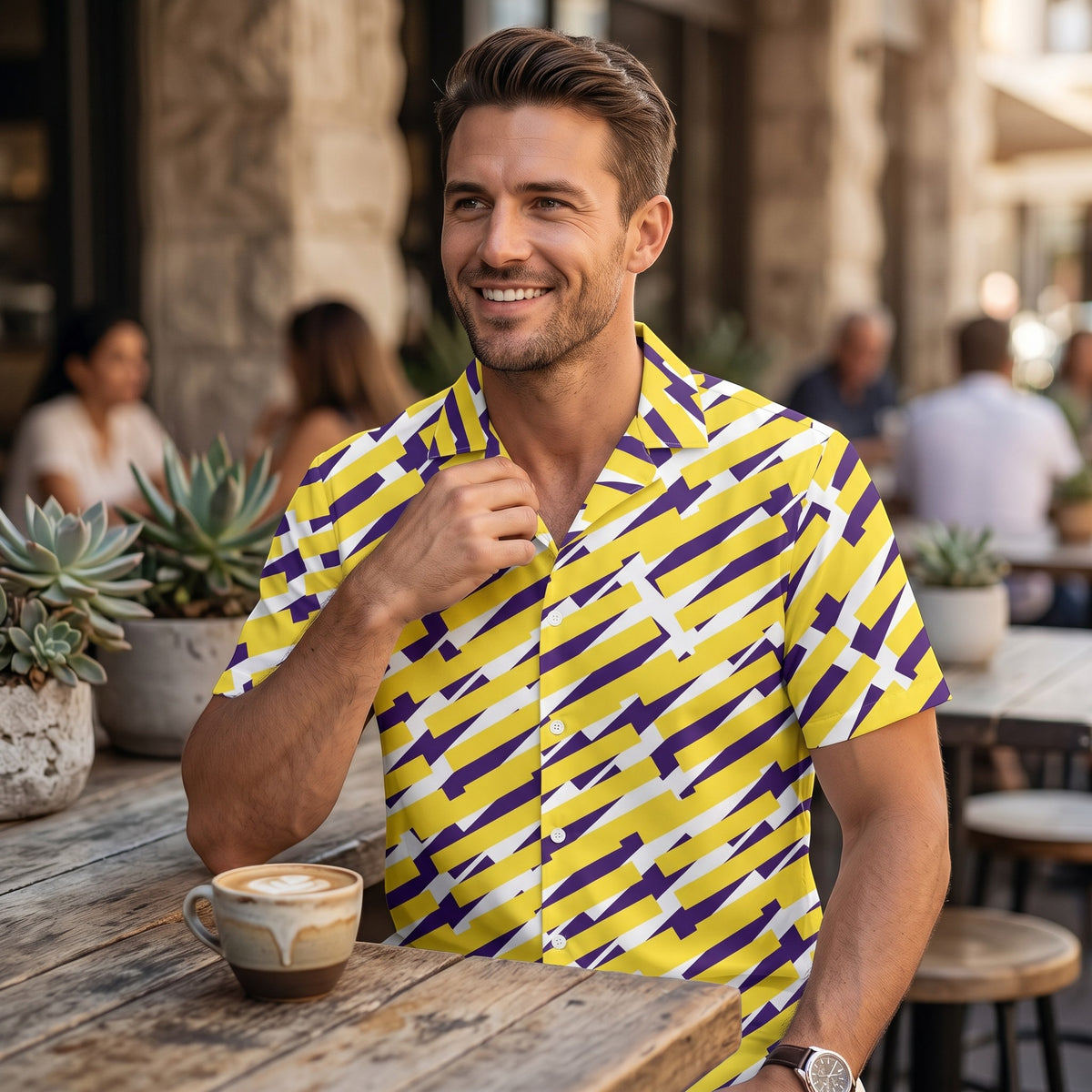 Good Wishes 365 short sleeve button down shirt with yellow and purple geometric print worn by a smiling man at a cafe