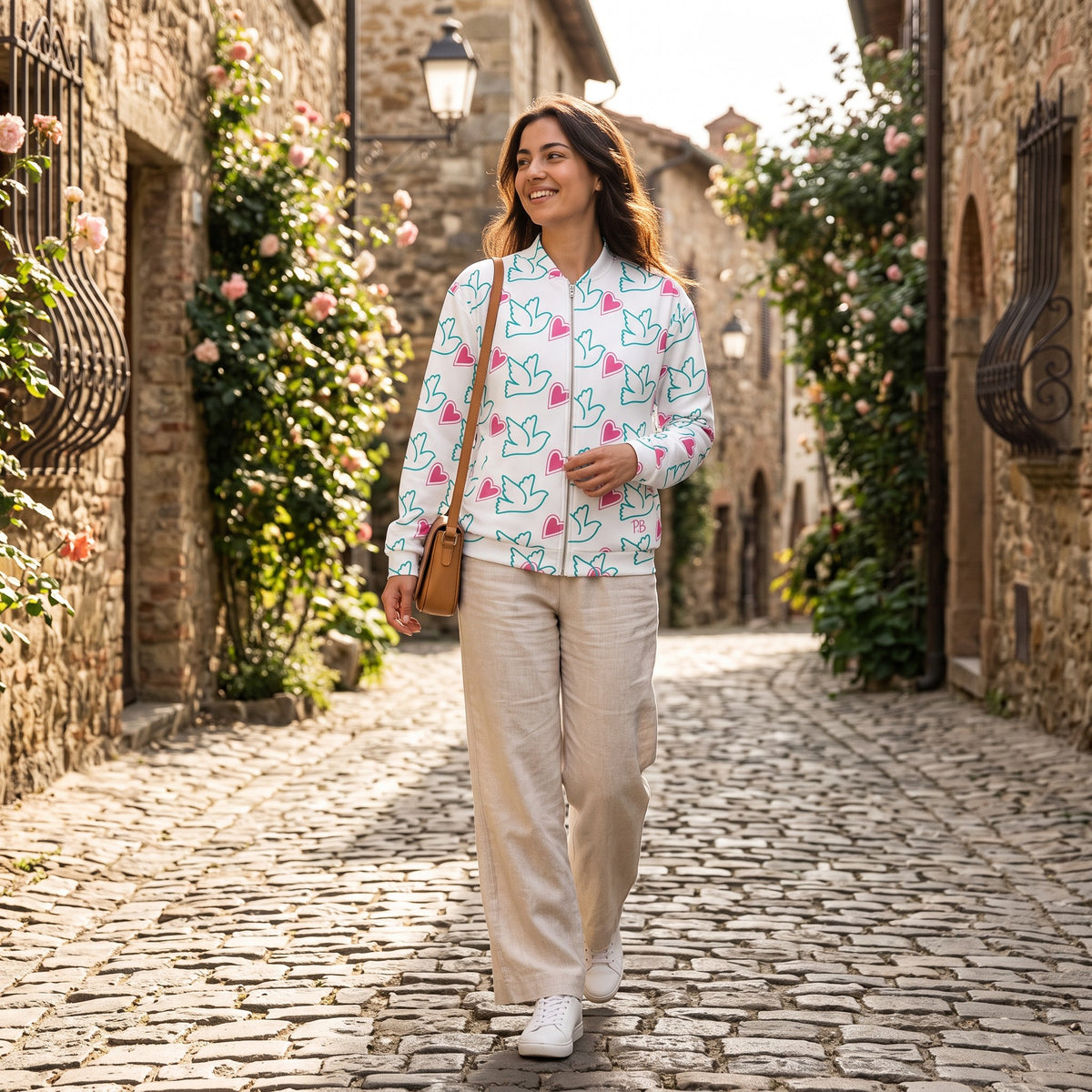 Good Wishes 365 unisex bomber jacket with peace sign and heart print worn by a woman on a cobblestone street
