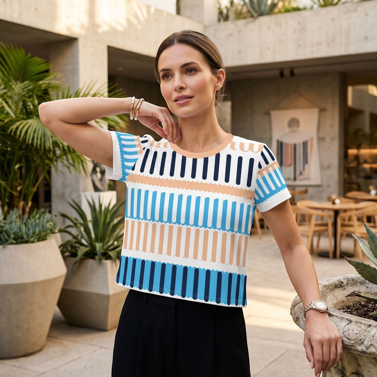 Good Wishes 365 crop tee with blue and peach coastal rhythm print, worn by a woman in a modern outdoor patio setting.