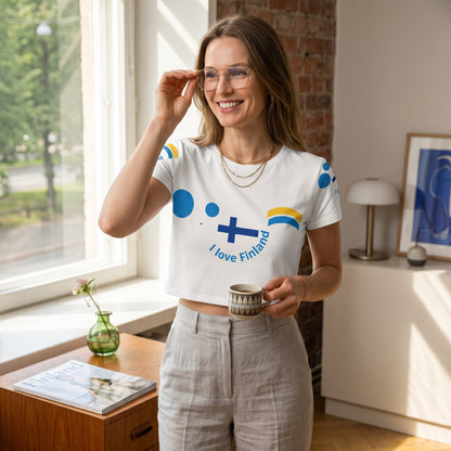Good Wishes 365 women's white crop tee with Finnish flag design, worn by a smiling woman in a bright room.
