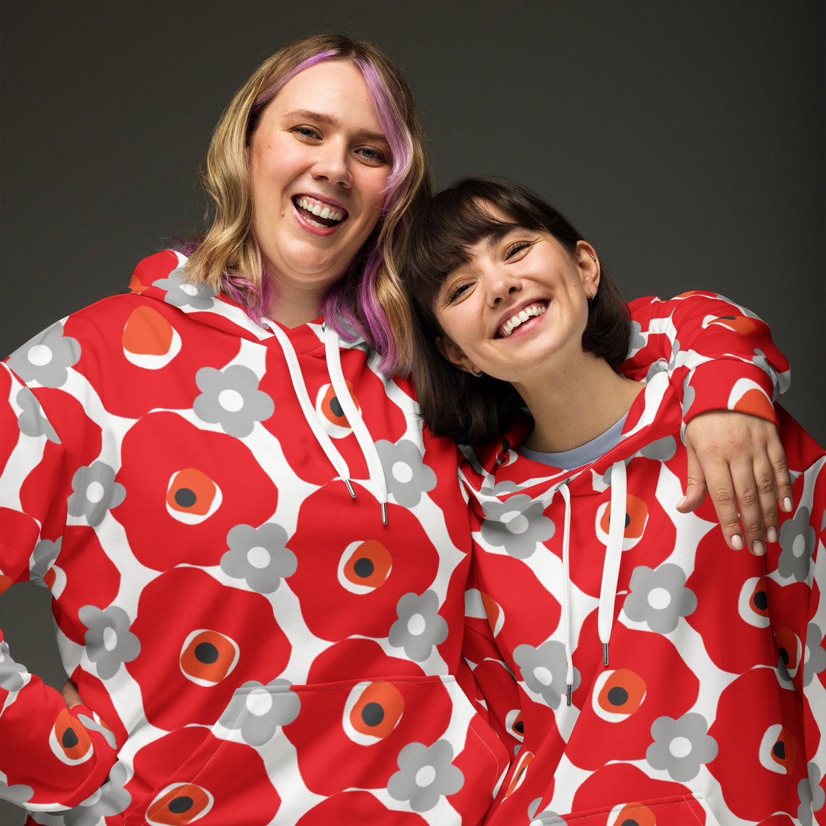 Two smiling women wearing Good Wishes 365 recycled hoodies with a vibrant red and gray floral all-over print