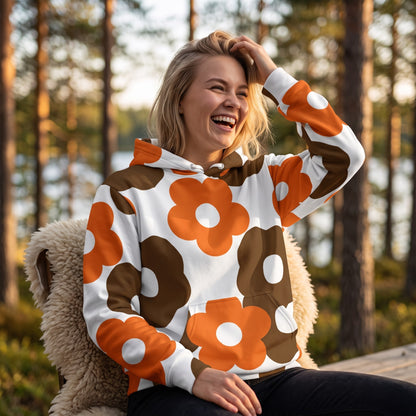 A smiling woman wearing a Good Wishes 365 recycled hoodie with a retro brown and orange floral print in a forest.