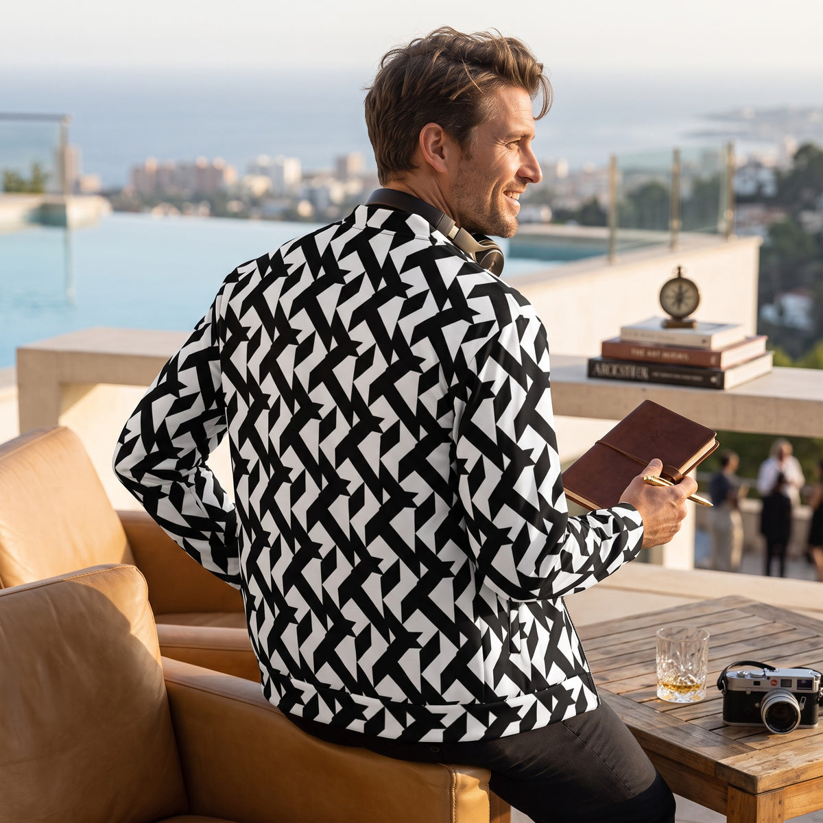 Good Wishes 365 unisex bomber jacket with a black and white geometric moon landing print, worn by a man on a terrace.