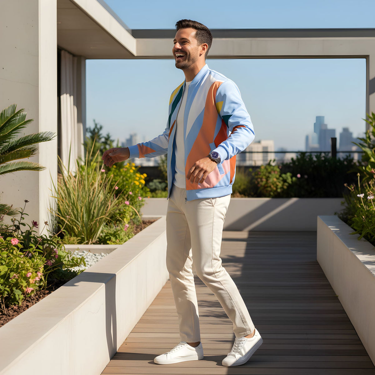 Man wearing a Good Wishes 365 abstract geometric bomber jacket in pastel blue and earth tones on a sunny rooftop.
