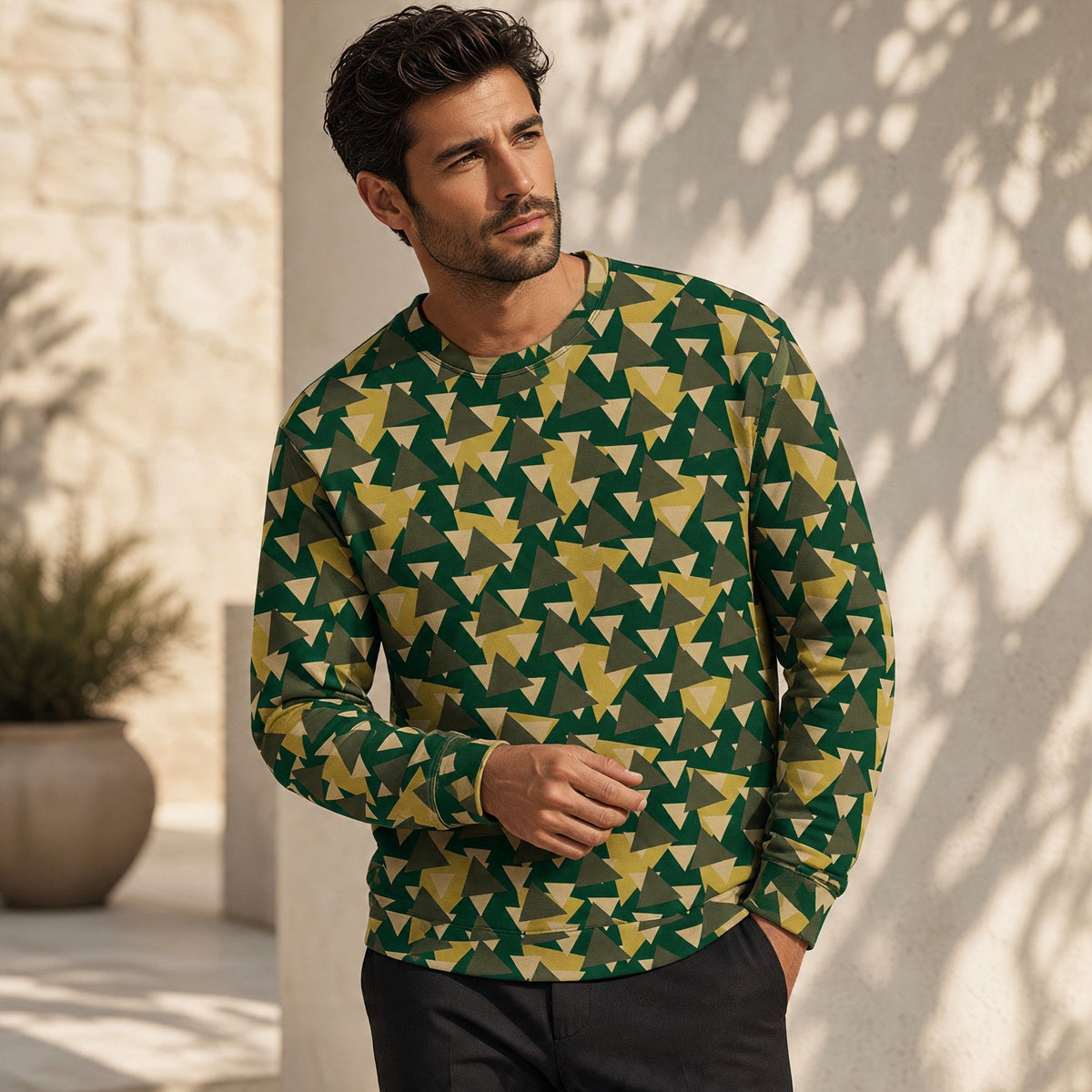 A man wearing a Good Wishes 365 recycled sweatshirt with a green and yellow geometric camo print in a sunny setting.