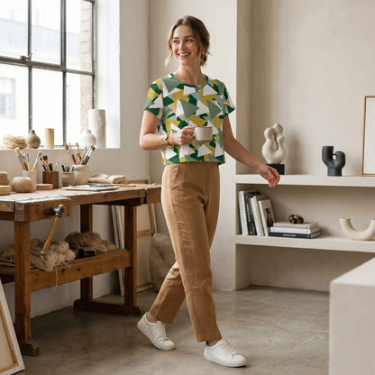 Good Wishes 365 woman wearing a green and white geometric print crop tee with tan trousers in a bright art studio.
