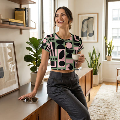 Good Wishes 365 crop tee with pink, green, and black geometric print worn by a smiling woman in a modern living room.