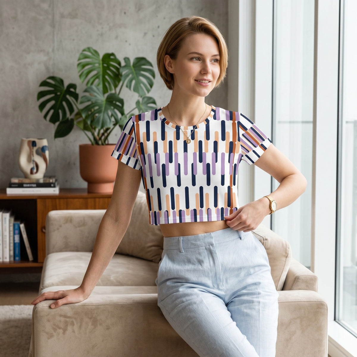 Good Wishes 365 crop tee with a purple, orange, and navy geometric print, worn by a woman in a bright living room.