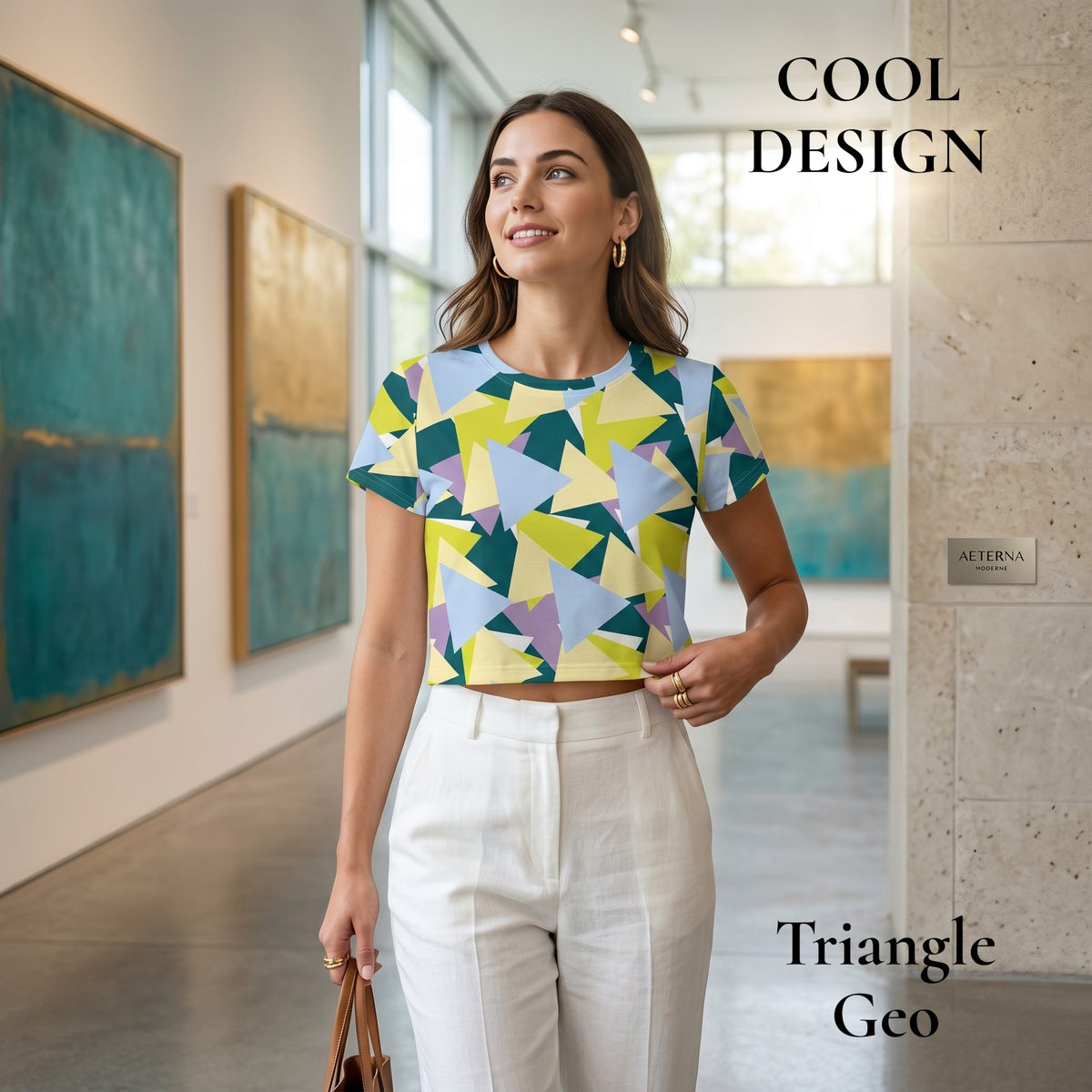 Good Wishes 365 crop tee with geometric triangle print in blue, yellow, and green, worn by a woman in an art gallery.
