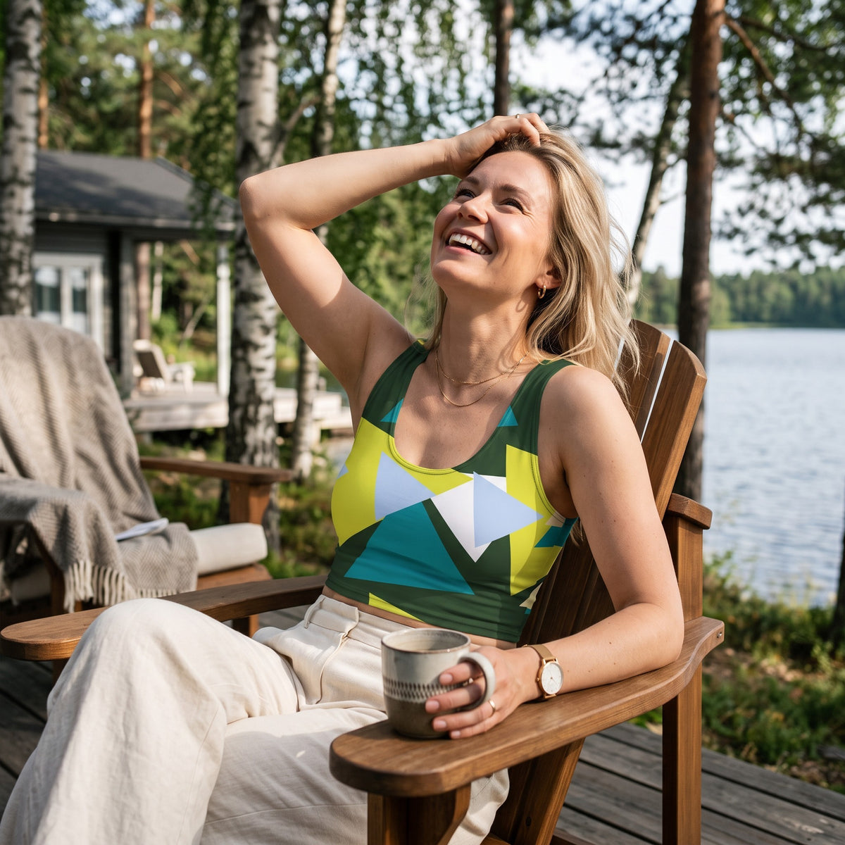 Woman wearing a Good Wishes 365 triangle geometric crop top in olive, yellow, and teal while sitting in a wooden chair.