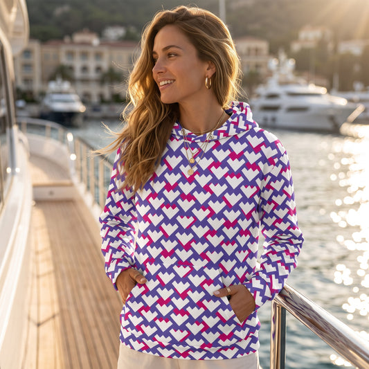 Good Wishes 365 unisex hoodie with purple and red geometric heart pattern, worn by a woman on a yacht deck at sunset.