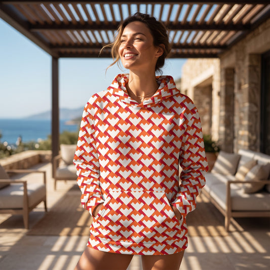 Woman wearing a Good Wishes 365 recycled unisex hoodie with a red and orange geometric heart pattern on a sunny patio.