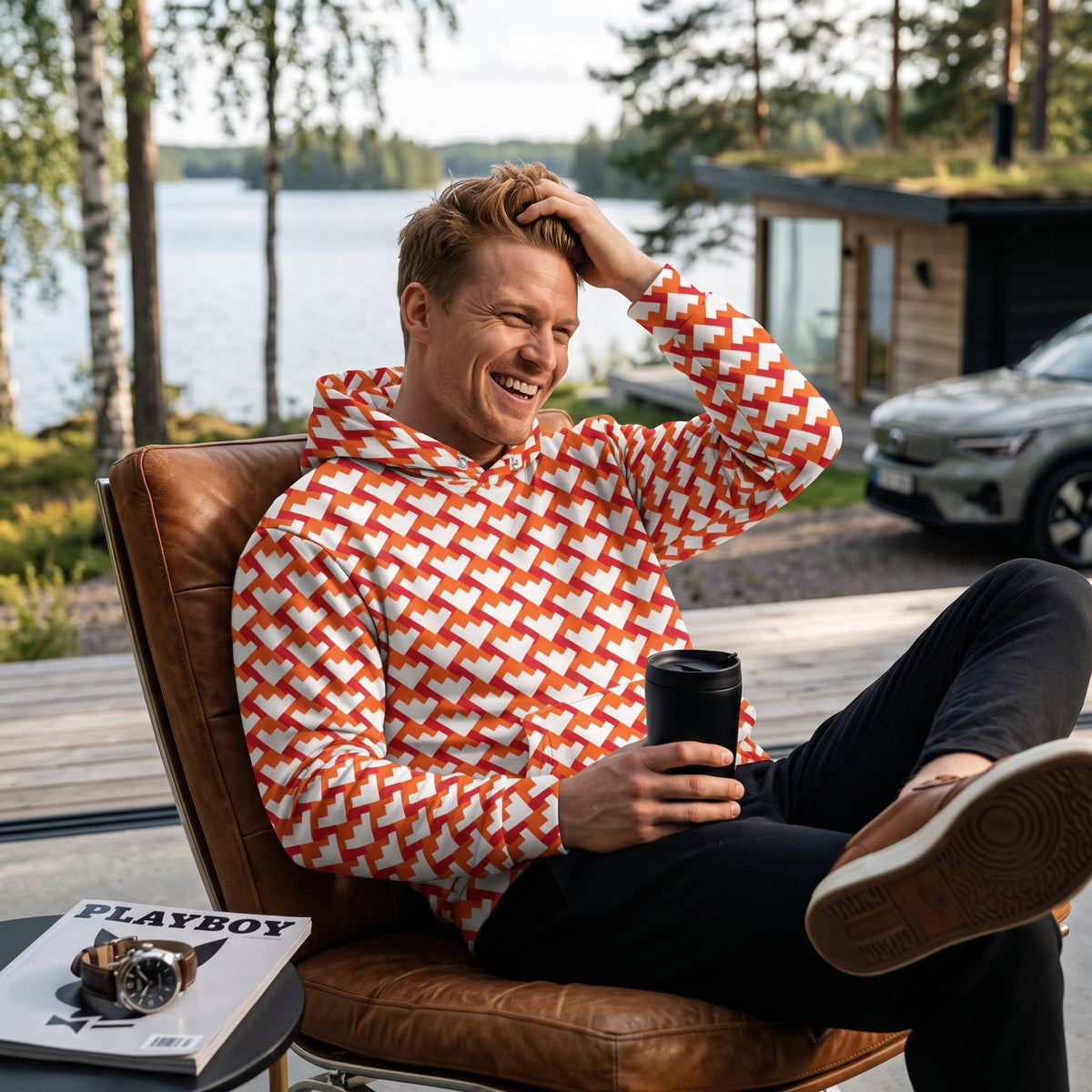Good Wishes 365 unisex hoodie with red and orange geometric heart pattern, worn by a man relaxing on a leather chair.