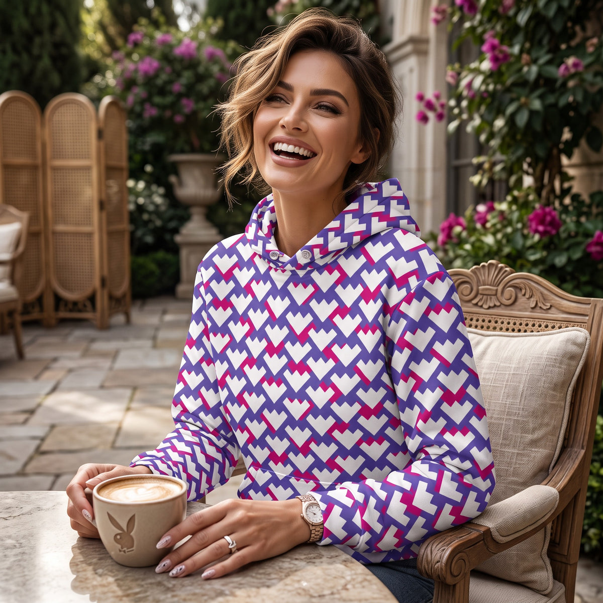 A smiling woman wearing a Good Wishes 365 recycled unisex hoodie with a purple, violet, and red geometric heart print.