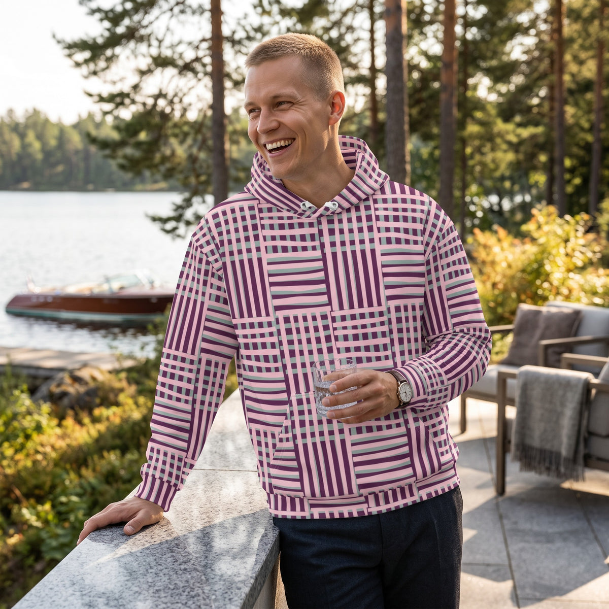 A man wearing a Good Wishes 365 recycled hoodie with a purple and blue geometric stripe pattern by a lakeside.