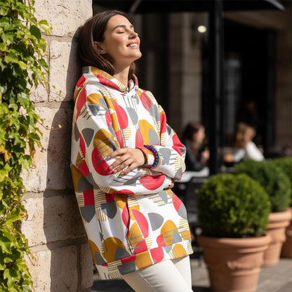 Good Wishes 365 recycled hoodie with rose red, mustard, and silver geometric print worn by a woman leaning on a wall.