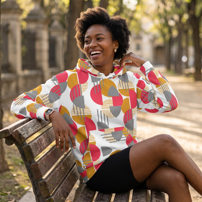 Good Wishes 365 recycled hoodie with rose red, mustard, and silver geometric print worn by a smiling woman on a bench