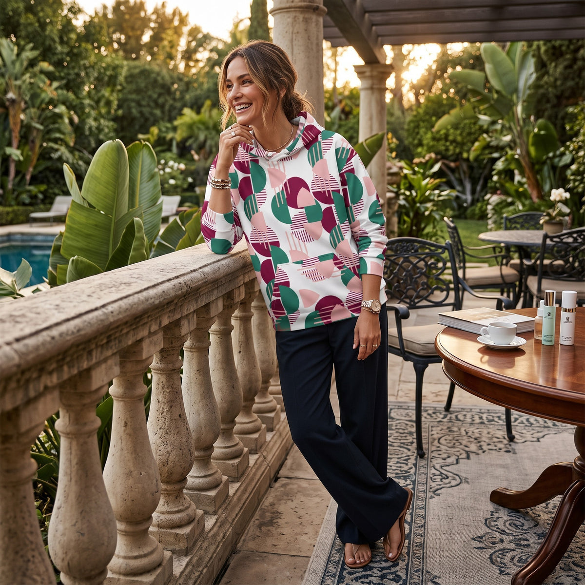 A woman wearing a Good Wishes 365 recycled hoodie with a pink, burgundy, and green geometric print on a patio.