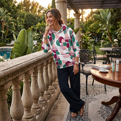 A woman wearing a Good Wishes 365 recycled hoodie with a pink, burgundy, and green geometric print on a patio.