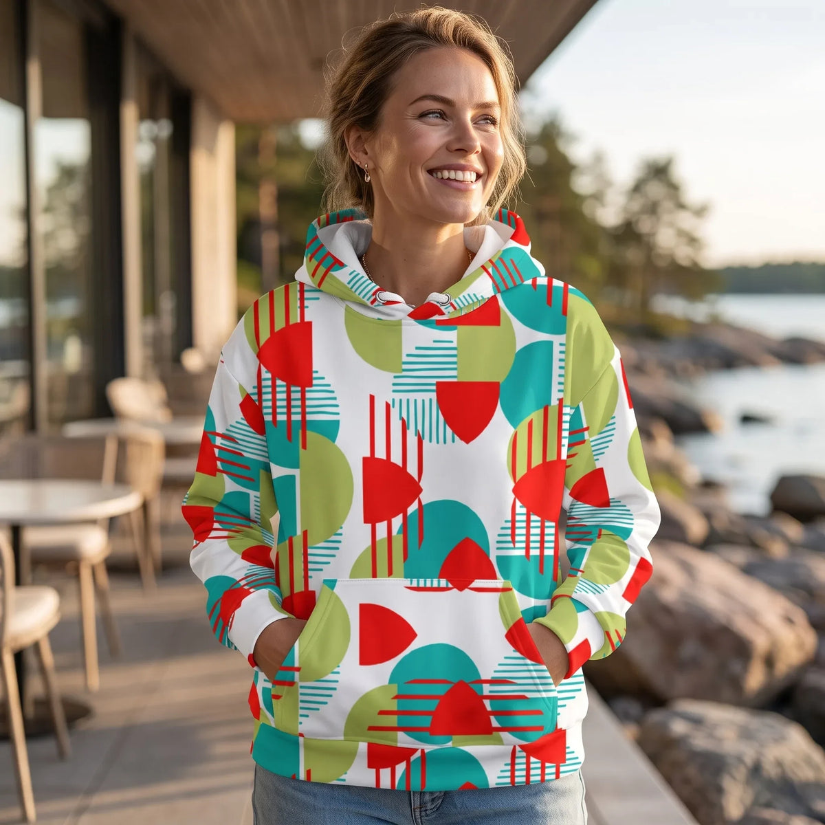 Good Wishes 365 recycled hoodie with a vibrant red, green, and teal geometric pattern worn by a smiling woman outdoors