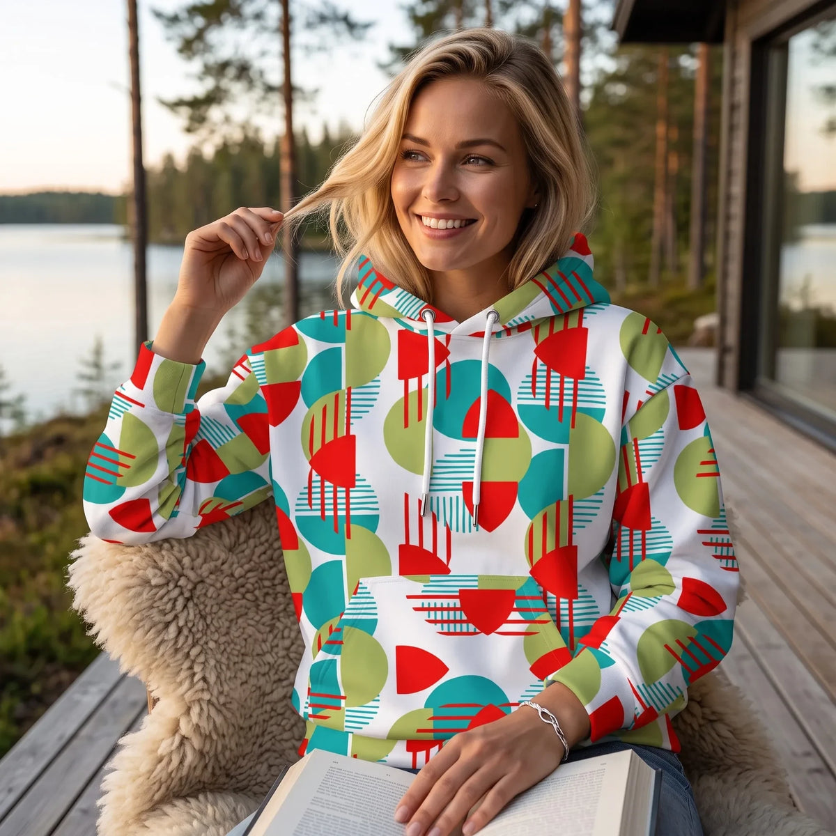 Good Wishes 365 recycled hoodie with red, green, and teal geometric pattern worn by a woman on a wooden deck