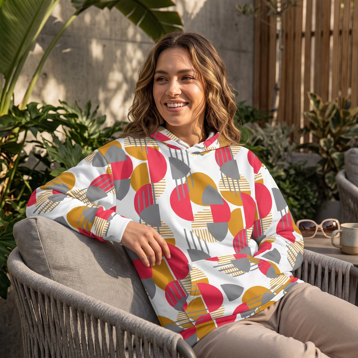 Good Wishes 365 recycled hoodie with rose red, mustard, and silver geometric print on a smiling woman outdoors