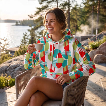 Good Wishes 365 recycled hoodie with red, green, and teal geometric print worn by a woman drinking coffee outdoors.