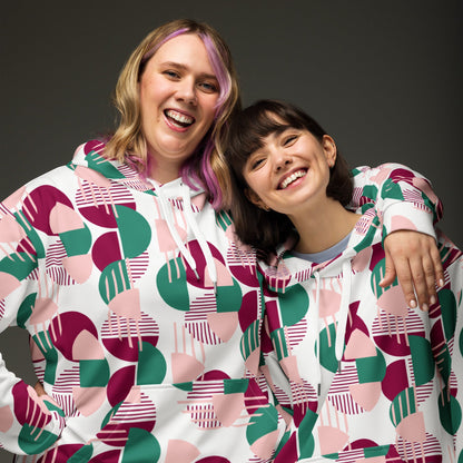 Two smiling women wearing Good Wishes 365 recycled hoodies with a pink, burgundy, and green geometric print.