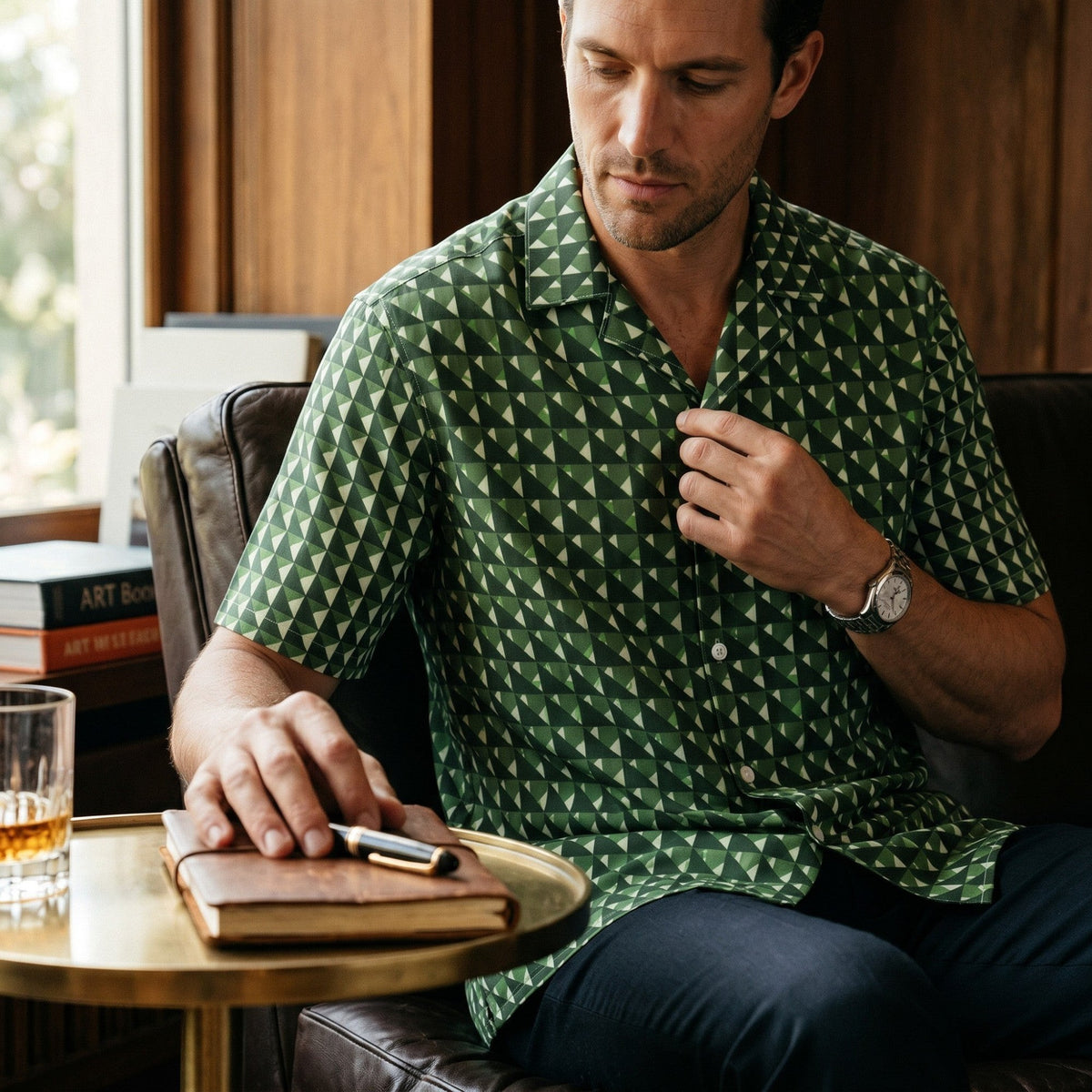 Good Wishes 365 men's short sleeve button shirt in green geometric triangle camo print, worn by a man in a lounge.