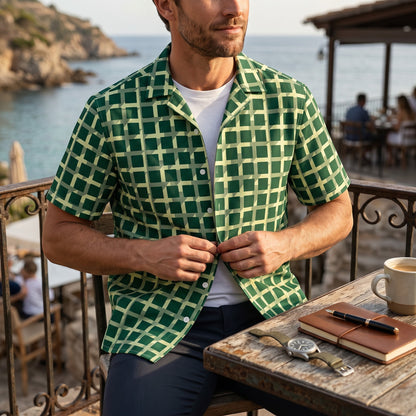 Good Wishes 365 men's green geometric checkered short sleeve button shirt worn over a white tee at a coastal cafe.