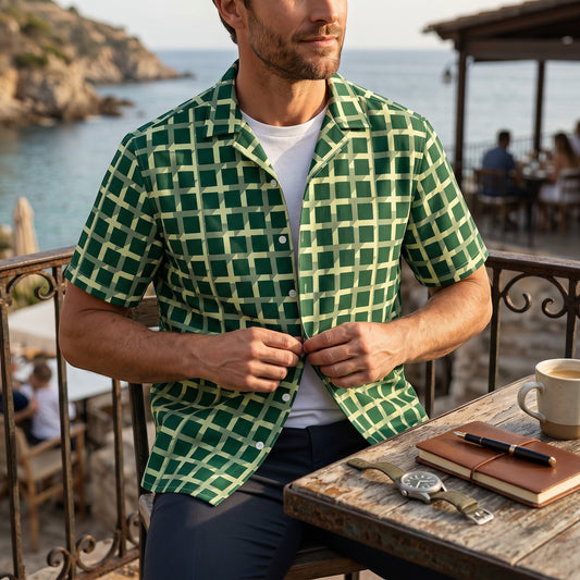 Good Wishes 365 men's green geometric checkered short sleeve button shirt worn over a white tee at a coastal cafe.