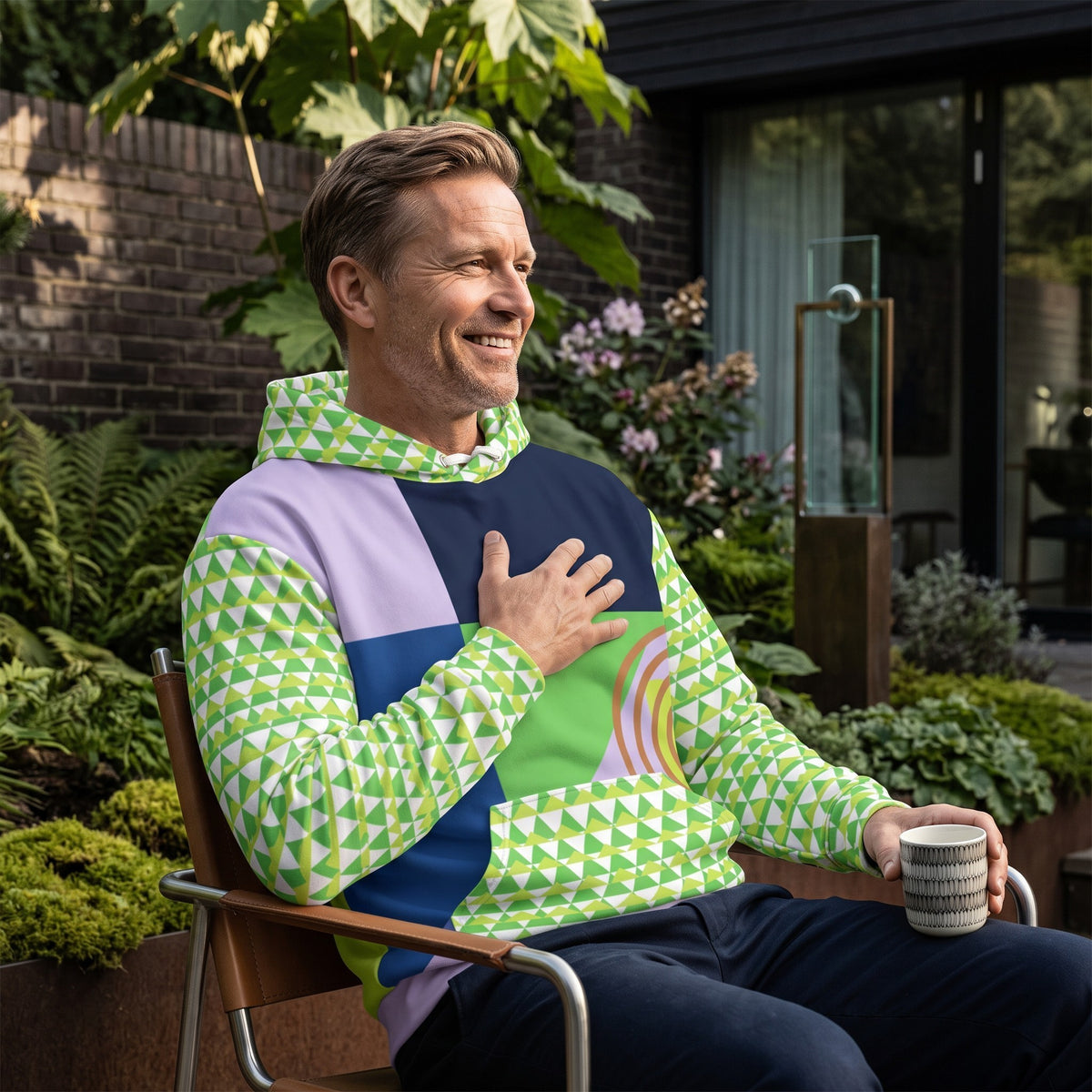 Good Wishes 365 men wearing a green and navy geometric 80s Memphis style recycled hoodie in a lush garden setting