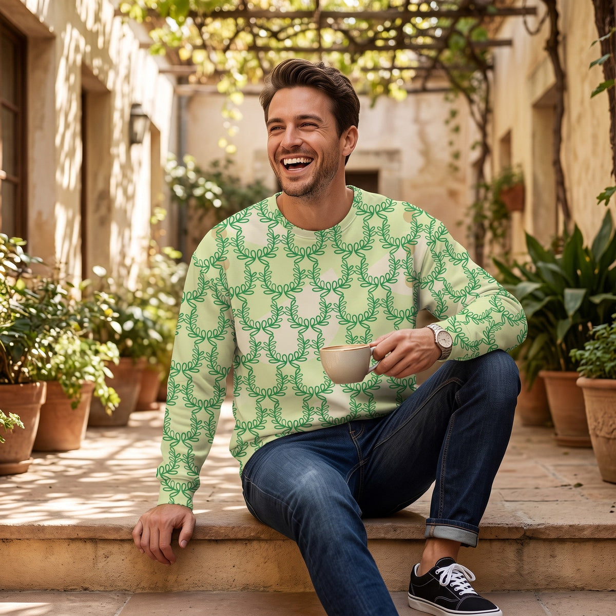 Man wearing a Good Wishes 365 green laurel leaf print recycled sweatshirt while sitting outdoors with a coffee.