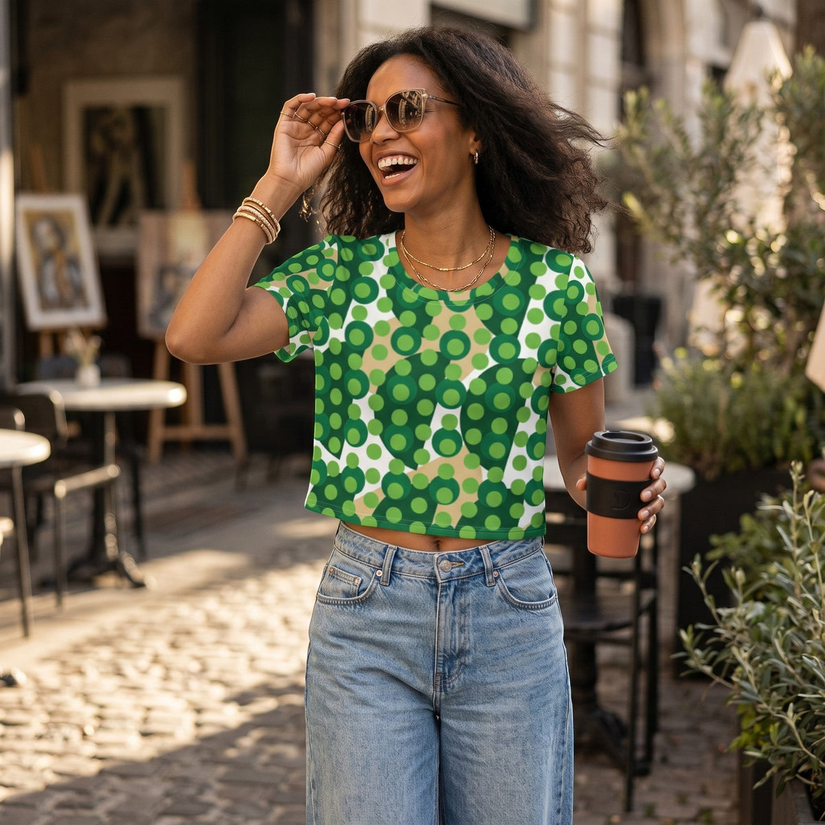 Good Wishes 365 crop tee with green and beige polka dot print worn by a smiling woman in a sunny outdoor cafe setting.