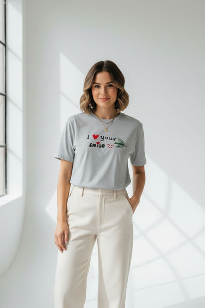 Good Wishes 365 grey crewneck t-shirt with I Love Your Smile graphic, worn by a woman with beige trousers.