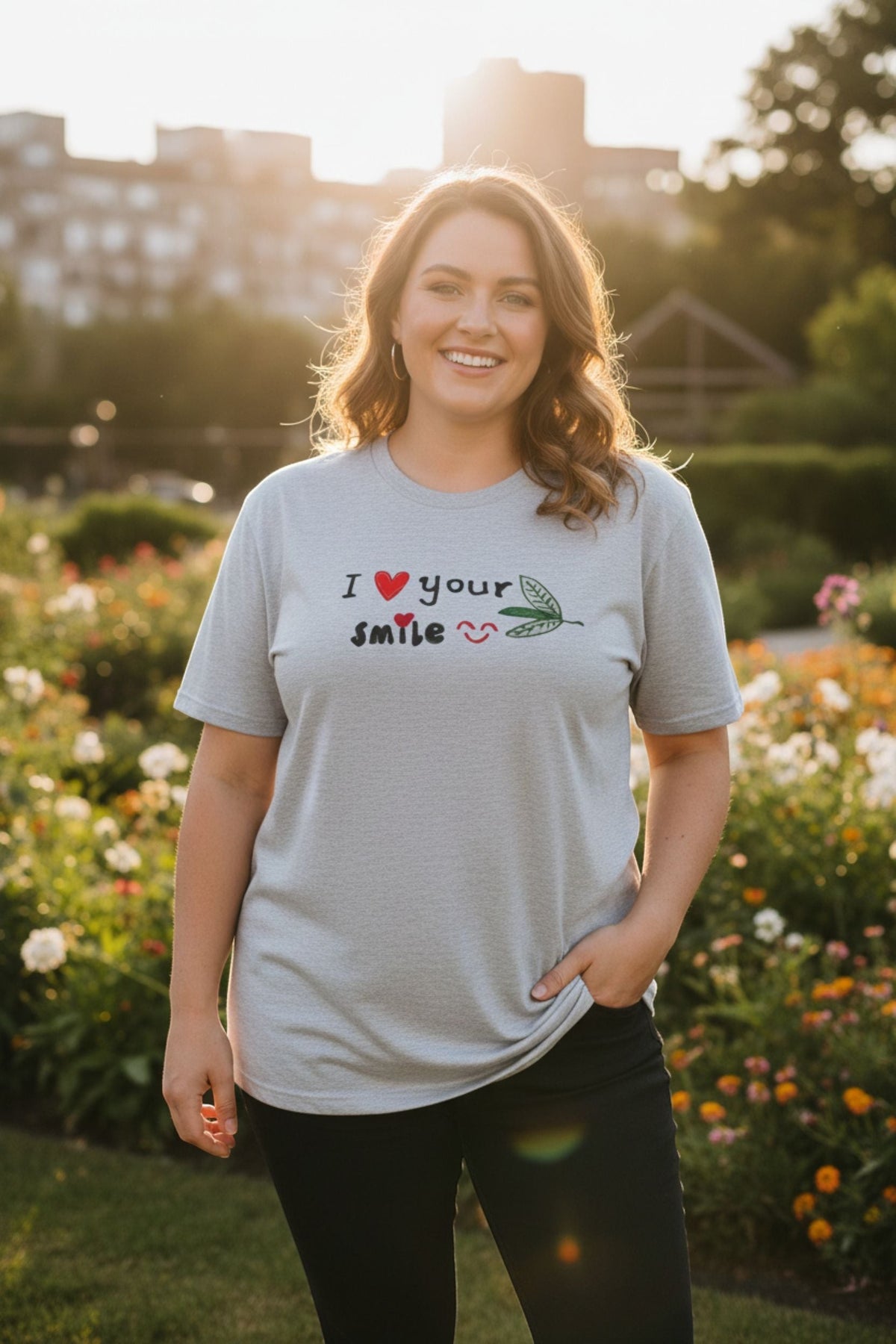 Good Wishes 365 unisex grey crewneck t-shirt with I Love Your Smile graphic, worn by a smiling woman in a garden.