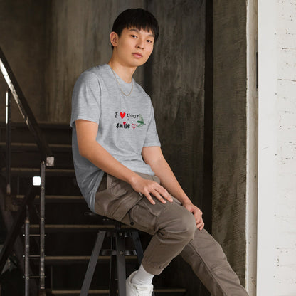 Good Wishes 365 grey unisex crewneck t-shirt with I Love Your Smile graphic worn by a man sitting on a stool.