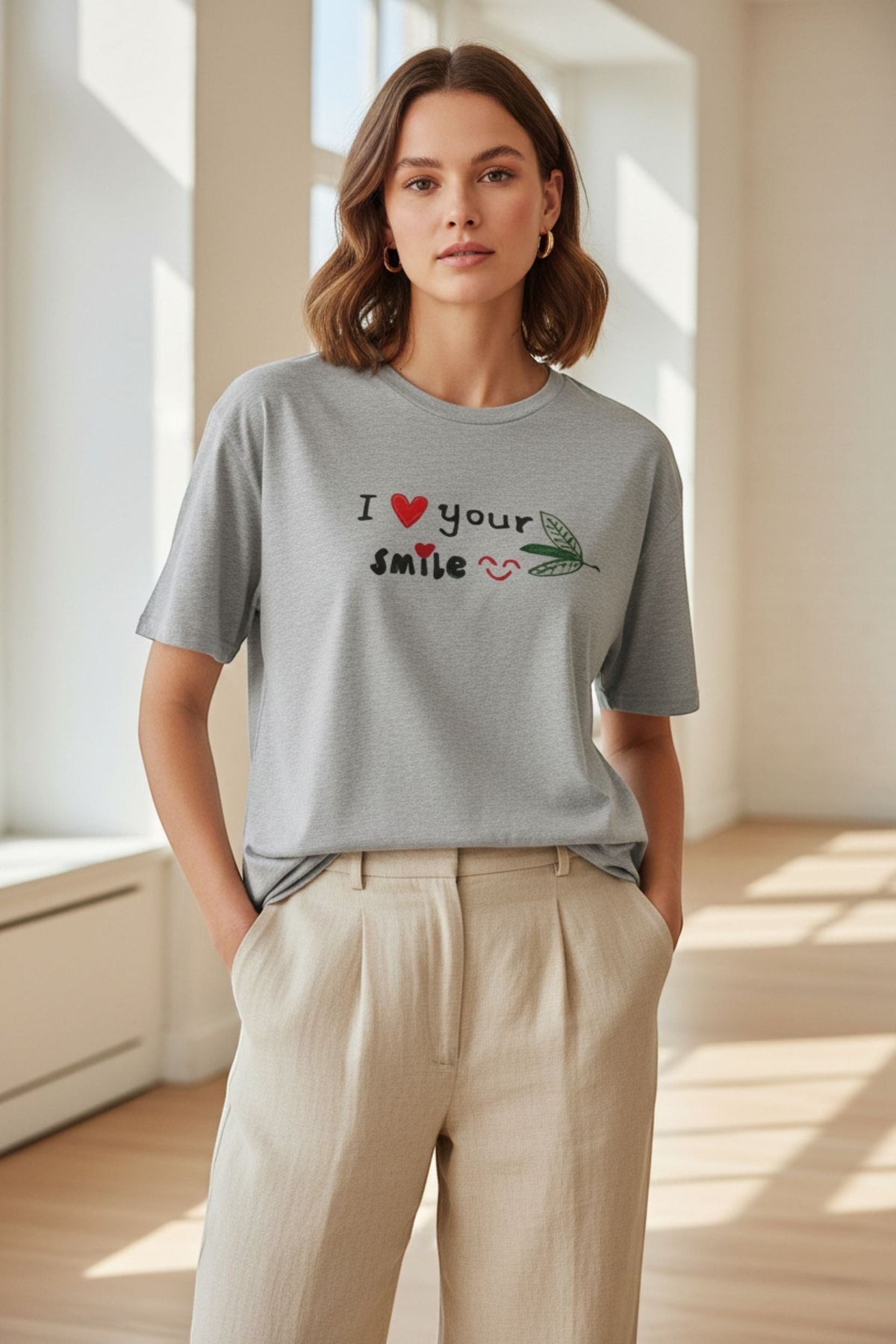 Good Wishes 365 grey unisex crewneck t-shirt with I Love Your Smile graphic, worn by a woman with beige trousers.