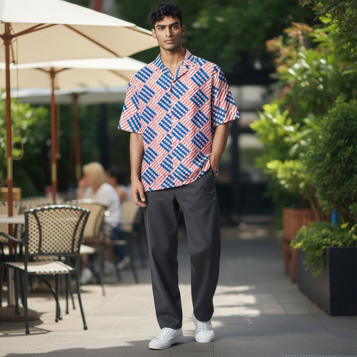 Good Wishes 365 men's oversized short-sleeve button shirt with a red and blue love pattern, worn in an outdoor cafe.