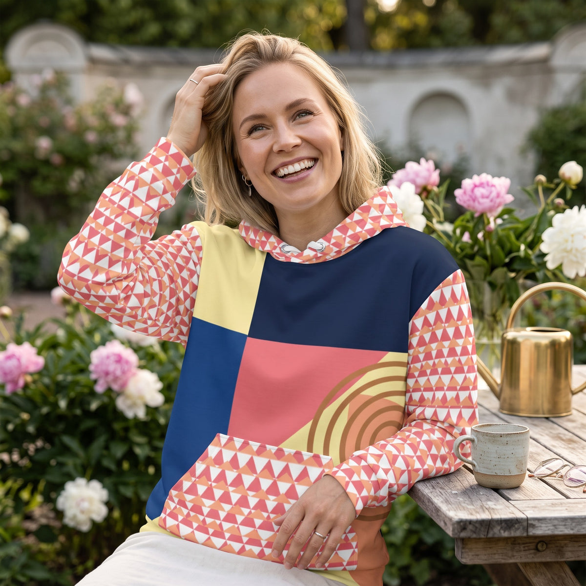 Good Wishes 365 recycled hoodie with 80s Memphis geometric print in navy, coral, and yellow worn by a smiling woman.
