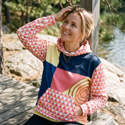 Good Wishes 365 recycled hoodie with 80s Memphis geometric print in navy, coral, and yellow worn by a smiling woman.