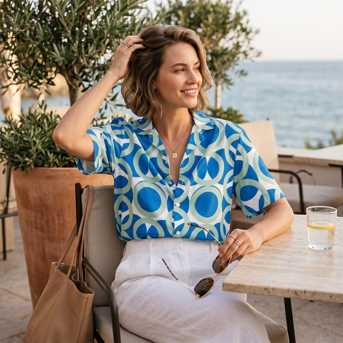 Good Wishes 365 navy blue retro geometric short sleeve button shirt worn by a woman at an outdoor cafe by the sea.