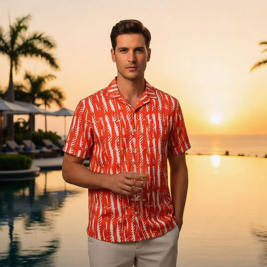 Good Wishes 365 unisex button shirt in orange with white abstract print, worn by a man at a tropical resort sunset.
