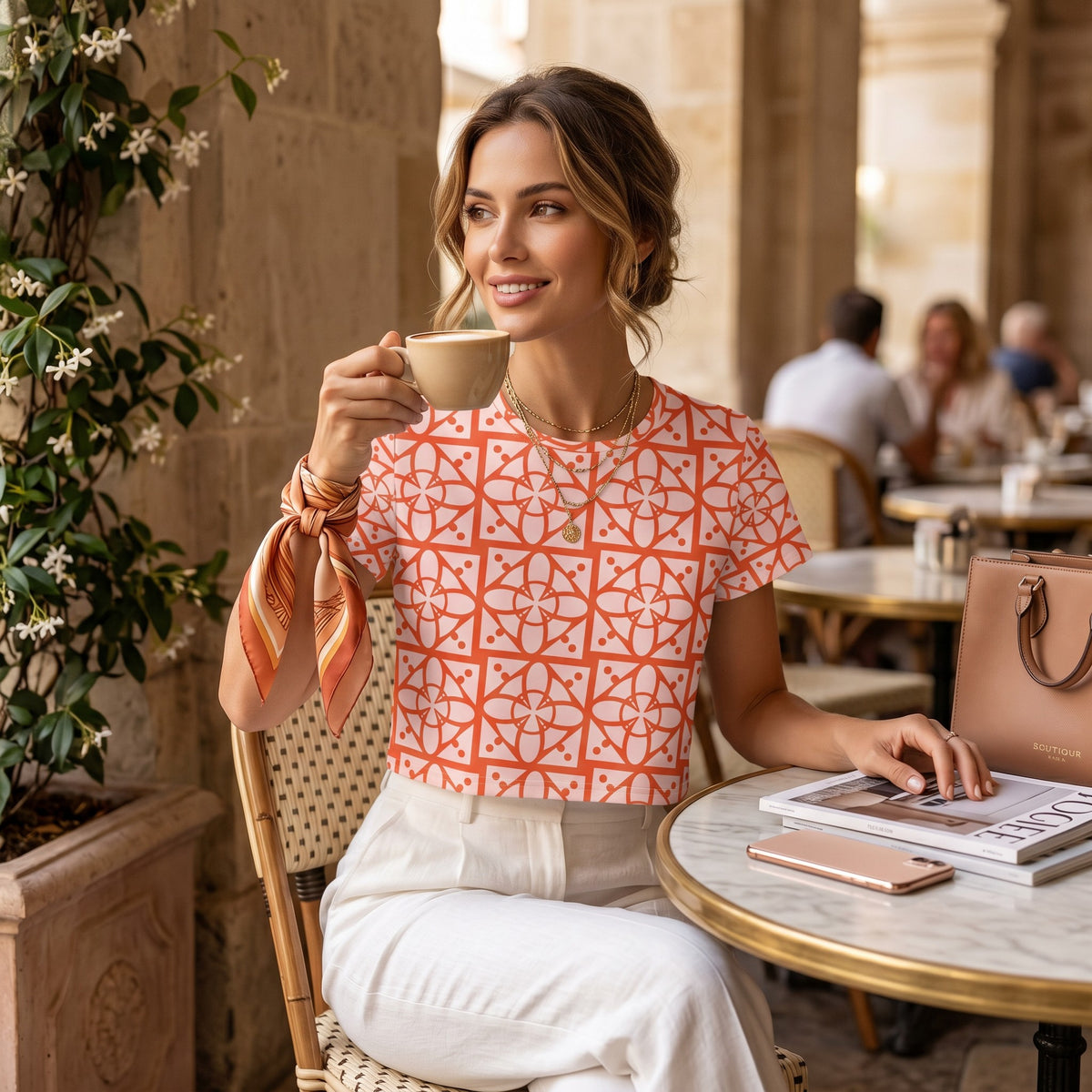 Good Wishes 365 crop tee with orange geometric print, worn by a woman drinking coffee at an outdoor cafe.