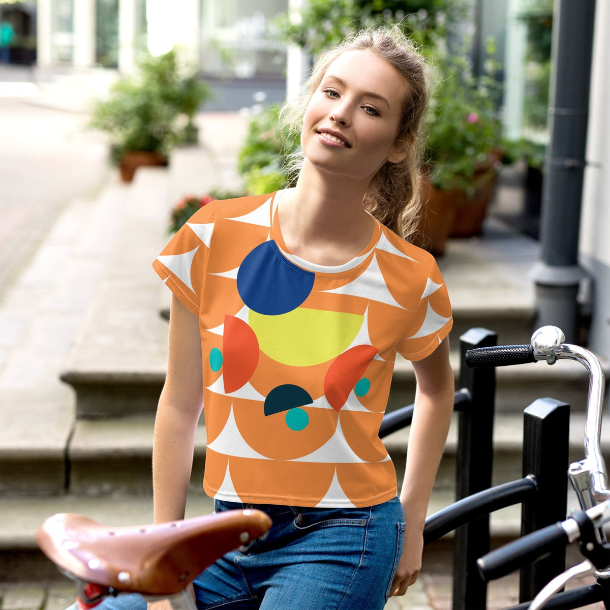 Good Wishes 365 orange crop tee with geometric mushroom graphic print worn by a woman outdoors with a bicycle