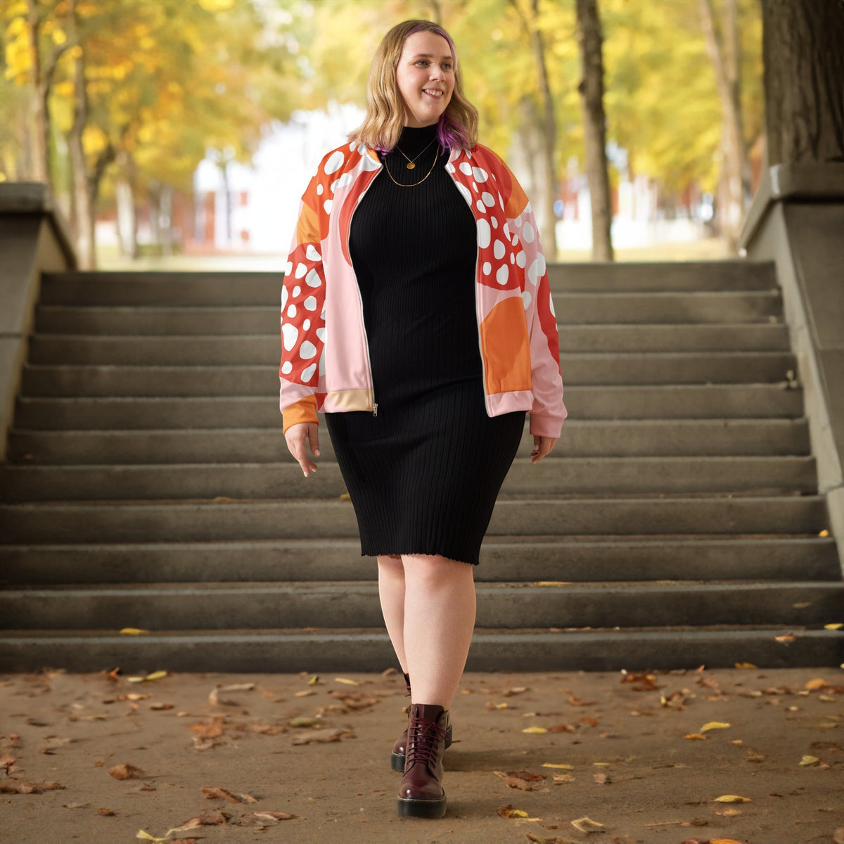 Good Wishes 365 unisex bomber jacket with orange strawberry print worn over a black dress on a park staircase