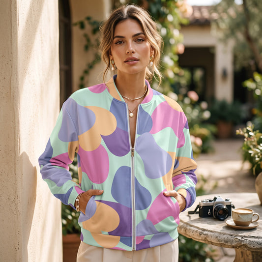 Woman wearing a Good Wishes 365 pastel bomber jacket with an all-over abstract print and silver zipper in a garden.
