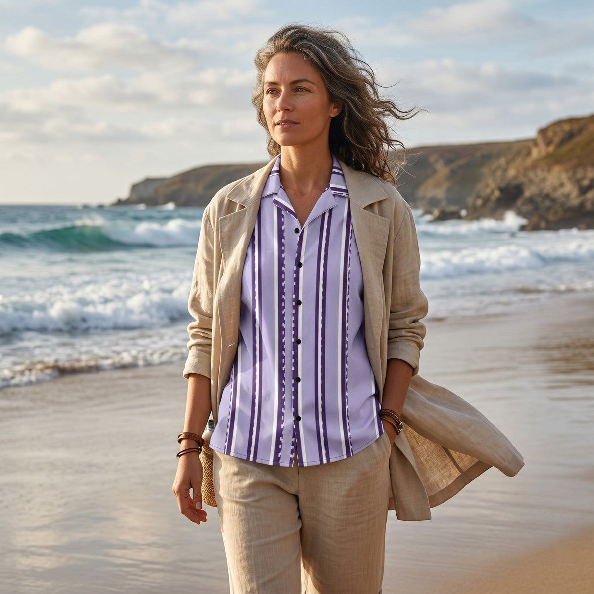 Good Wishes 365 retro pastel violet striped short sleeve button shirt worn by a woman on a beach in a linen outfit.