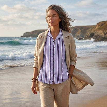 Good Wishes 365 retro pastel violet striped short sleeve button shirt worn by a woman on a beach in a linen outfit.