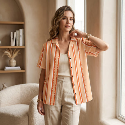 Good Wishes 365 retro pastel peach striped short sleeve button shirt worn by a woman in a bright, modern interior.